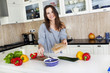 Portrait of a young woman doing a salad in her kitchen, while co