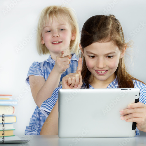 Photo: Two cute girlfriends learning with books and touchpad Two cute girlfriends learning with books and touchpad