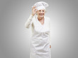 senior woman cook doing an excellent symbol against a grey backg senior woman cook doing an excellent symbol against a grey backg