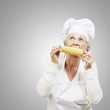 senior woman cook eating a corncob against a grey background senior woman cook eating a corncob against a grey background
