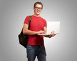 portrait of young man holding laptop and wearing backpack over g