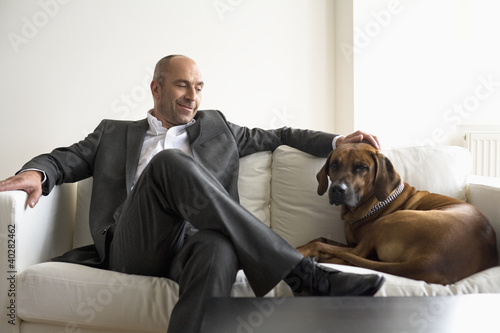 Photo: Businessman sitting on sofa with dog Businessman sitting on sofa with dog