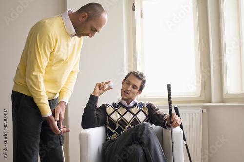 Photo: Man holding golf ball while other man holding gold club Man holding golf ball while other man holding gold club