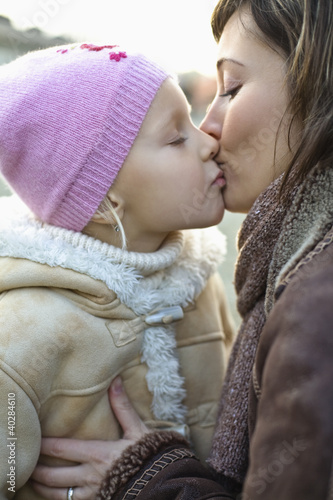 Photo: Mother kissing daughter, side view, close-up Mother kissing daughter, side view, close-up