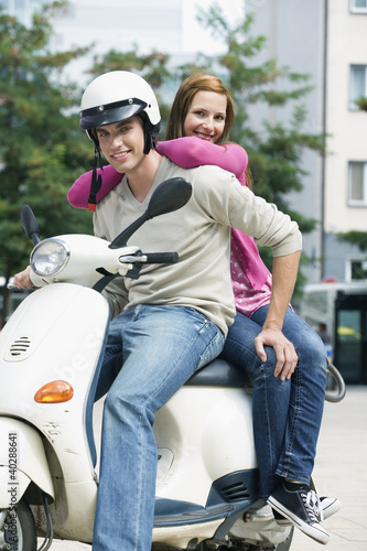 Photo: Young couple sitting on motor scooter, smiling Young couple sitting on motor scooter, smiling