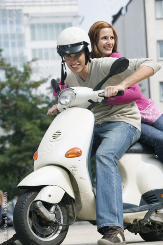 Photo: Young couple sitting on motor scooter, smiling Young couple sitting on motor scooter, smiling