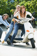 Young man pushing young women on motor scooter, smiling
