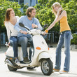 Young couple sitting on motor scooter while friend smiling