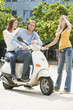 Young couple sitting on motor scooter while friend smiling