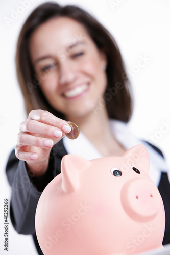 Photo: Close-up of young woman putting coin into a piggy bank Close-up of young woman putting coin into a piggy bank