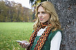 Young woman leaning by tree trunk, listening to MP3 player