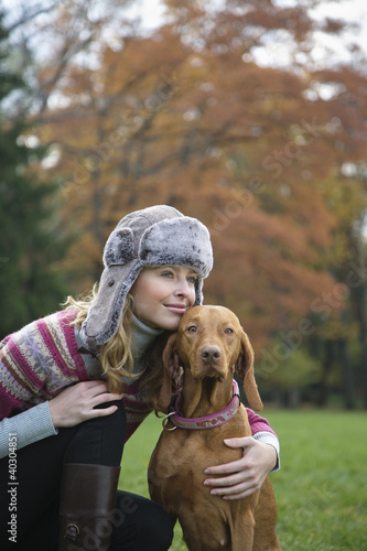 Photo: Young woman smiling with dog in garden, looking away Young woman smiling with dog in garden, looking away