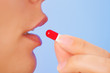 Young woman taking red and white bolus (capsule), macro view