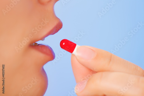 Photo: Young woman taking red and white bolus (capsule), macro view Young woman taking red and white bolus (capsule), macro view