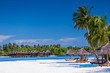 Palm trees over sandy tropical beach with villas over water