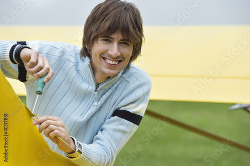 Photo: Young man screwing hook in airplane, smiling, portrait Young man screwing hook in airplane, smiling, portrait