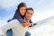 Photo: Man giving piggyback ride to girlfriend on the beach Man giving piggyback ride to girlfriend on the beach