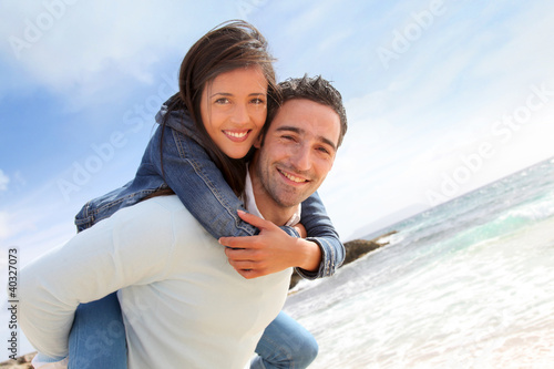 Photo: Man giving piggyback ride to girlfriend on the beach Man giving piggyback ride to girlfriend on the beach