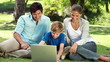 Happy family looking at a laptop while sitting on the grass