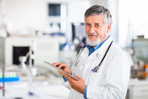 Photo: Senior doctor using his tablet computer at work (color toned ima Senior doctor using his tablet computer at work (color toned ima