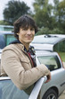 Photo: Young man standing by car, smiling, portrait Young man standing by car, smiling, portrait