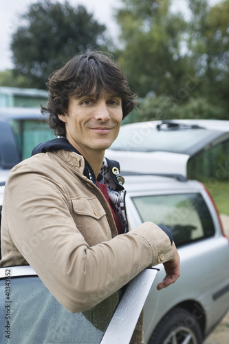Photo: Young man standing by car, smiling, portrait Young man standing by car, smiling, portrait