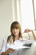 Young woman holding magazine and glasses, contemplating