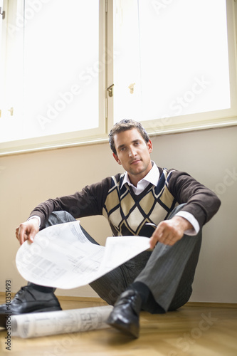 Photo: Businessman sitting on hardwood floor, holding blue print Businessman sitting on hardwood floor, holding blue print
