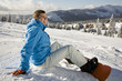 Young man sitting on snow, smiling, side view
