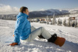 Young man sitting on snow, smiling, side view
