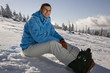 Young man sitting on snow, smiling, side view