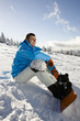 Young man sitting on snow, smiling, portrait