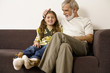 Senior man sitting with granddaughter on sofa, smiling