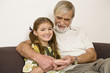 Senior man sitting with granddaughter on sofa, smiling