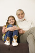 Senior man sitting with granddaughter on sofa, smiling