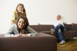 Girl sitting on woman's back while man relaxing in background