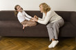 Senior woman sitting with granddaughter on sofa, smiling