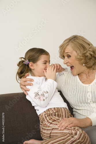 Photo: Senior woman sitting with granddaughter on sofa, smiling Senior woman sitting with granddaughter on sofa, smiling