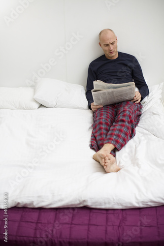 Photo: Mid adult man reading newspaper on bed Mid adult man reading newspaper on bed