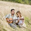 Mid adult couple sitting on field, man playing guitar