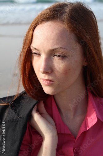 Foto: Pretty redhead woman at the beach, holding her jacket Pretty redhead woman at the beach, holding her jacket