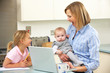Mother with children using laptop in kitchen