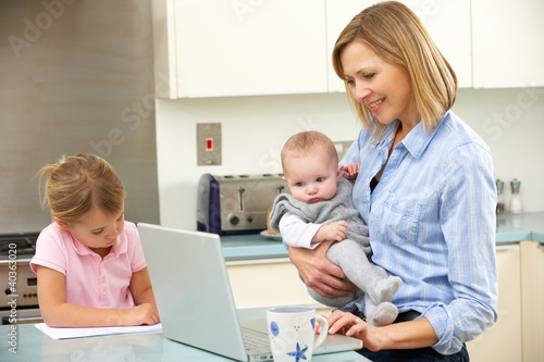 Photo: Mother with children using laptop in kitchen Mother with children using laptop in kitchen