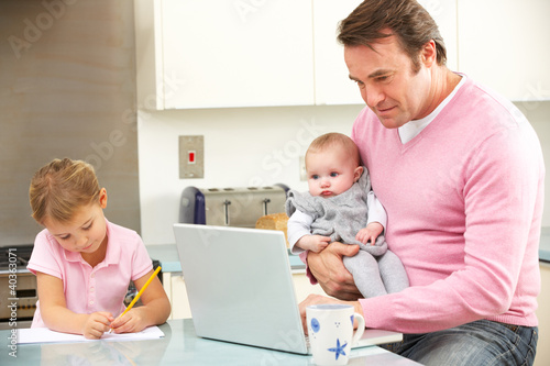 Photo: Father with children using laptop in kitchen Father with children using laptop in kitchen