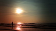 Woman on the beach at sunset. Watercraft in the background.