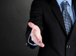 Businessman giving his hand for a handshake on black background