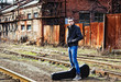 Young man with guitar case waiting for train among industrial ru Young man with guitar case waiting for train among industrial ru