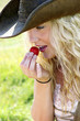A woman with cowboy hat eating a strawberry.