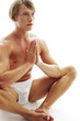 A shirtless man in white underwear sitting on the floor praying.
