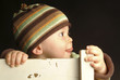 A boy in sweater and hat biting a chair.